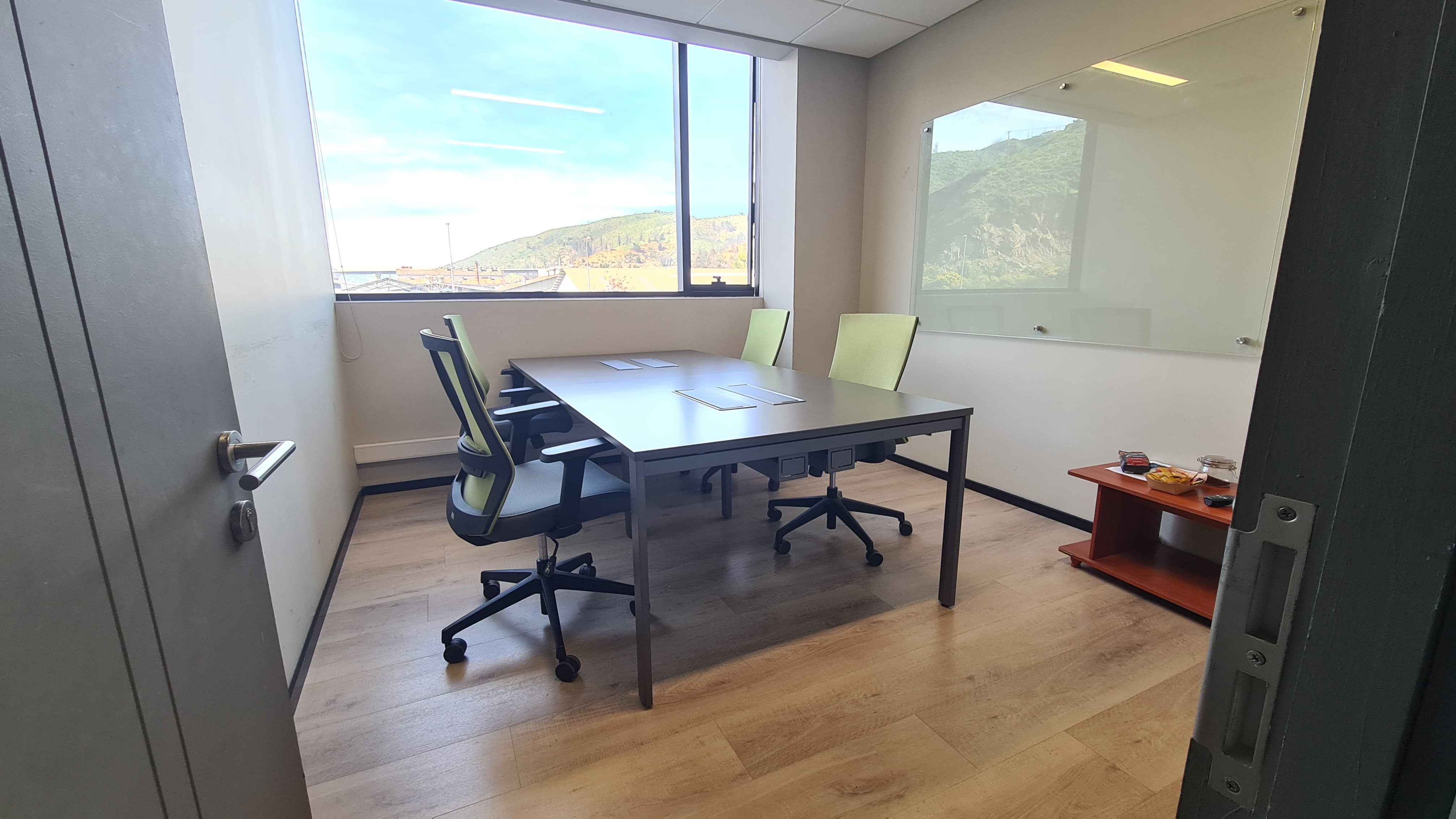 Oficina privada Cowork V21 con escritorios, sillas verdes y ventanal
